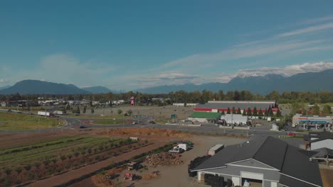 hermosa granja en el borde de la autopista en el valle de chilliwack principios de invierno muchos verdes marrones cielo azul cordillera en el fondo reverso aéreo que revela más cultivos y edificios agrícolas
