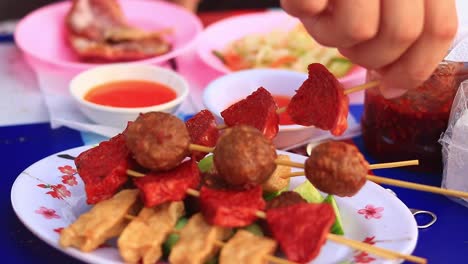 close up video to a plate full of khmer or cambodian streetfood skewers while a tourist is trying them out