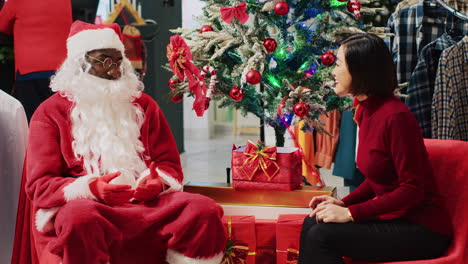 Asian-woman-engaging-in-conversation-with-employee-impersonating-Santa-Claus-during-festive-Christmas-shopping-experience.-Customer-receiving-xmas-present-from-worker-in-fashion-shop