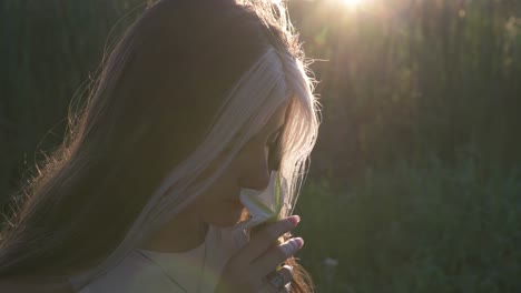 beautiful young woman smelling flower in nature illuminated by sun at sunset