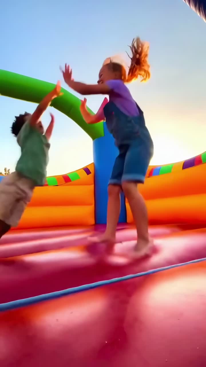 Vídeo de ângulo baixo de crianças alegres pulando em um castelo inflável colorido sob um céu limpo