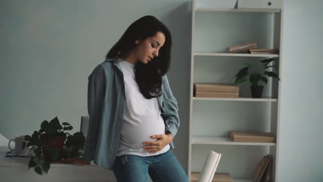 young pregnant business woman with headache and tired from work takes a break stroking her belly at home