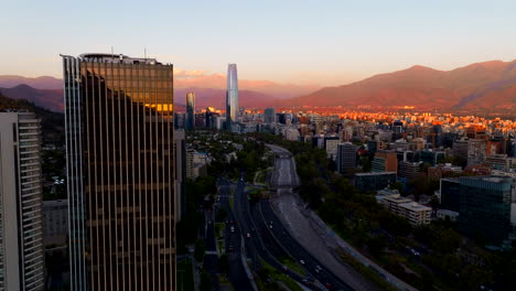 aerial view of city skyline with gran torre santiago at sunset, vibrant cityscape glowing as traffic flows through the urban streets against a mountain backdrop