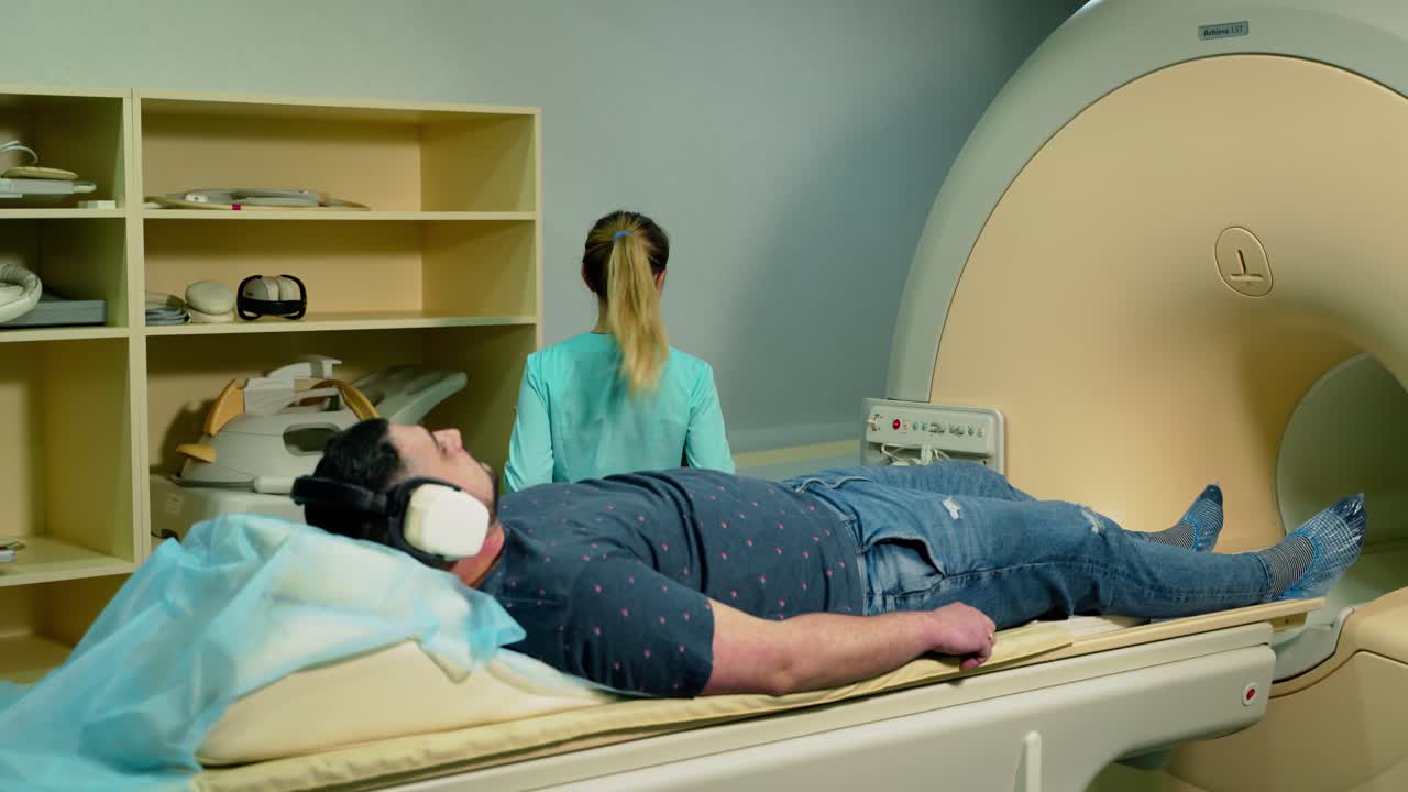 Man in headphones lying on a bed in clinic. Nurse takes of medical equipment from the patient. Modern medical equipment in the hospital.