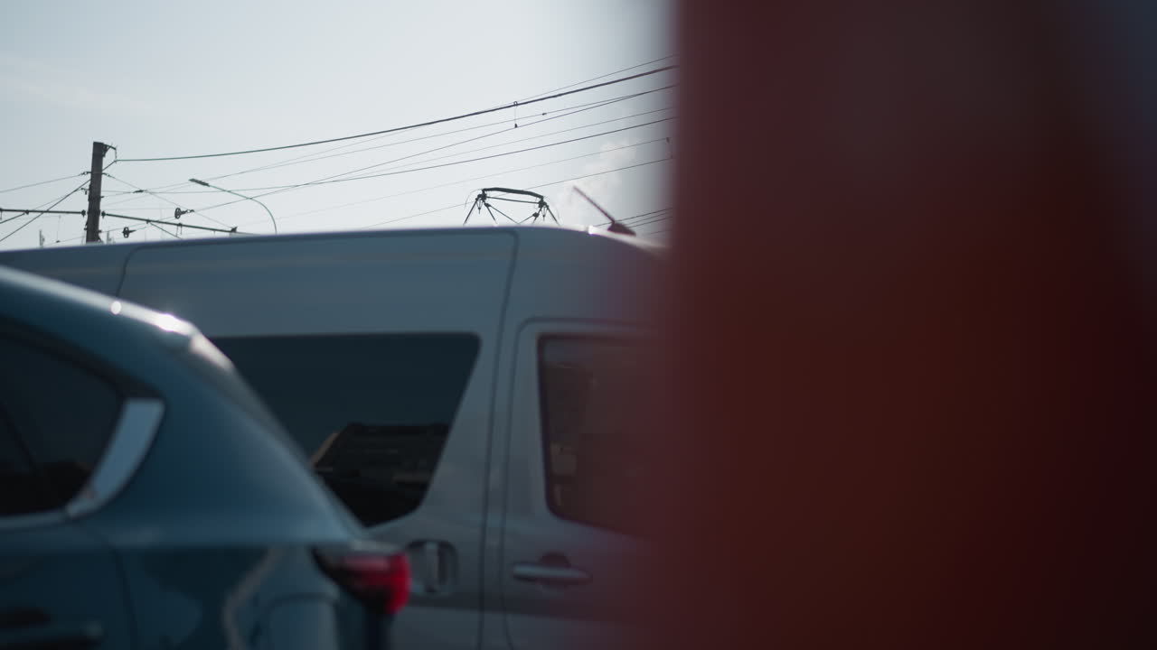 Corner view city bus at stop during winter commute, cars moving past busy street, modern buildings, overhead wires, cold daylight, passengers visible in windows, urban transport scene