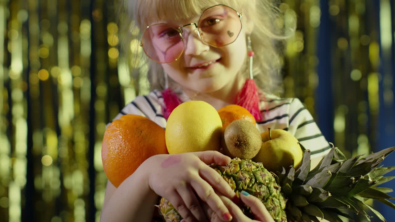 Close-up van meisje met stijlvolle zonnebril dat poseert, naar de camera kijkt en fruit in haar handen heeft