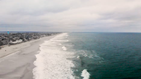 aerial flyover of the a small barrier island beach town along the coast as waves crash into the shore