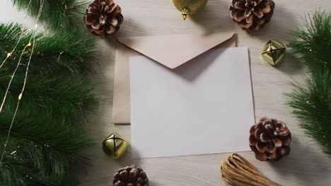 video of christmas decorations with white card and beige envelope on wooden background