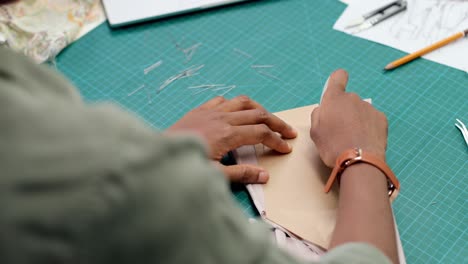 vista superior de la mujer sastre sentada en la mesa dibujando líneas en el boceto de la ropa en el taller de costura