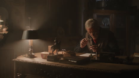 older passionate man evaluates an old silver skull watch in his office at night