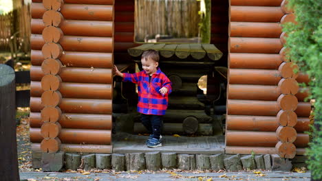 happy kid wearing checkered shirt stands at the wooden log gazebo. lovely child outdoors in autumn.