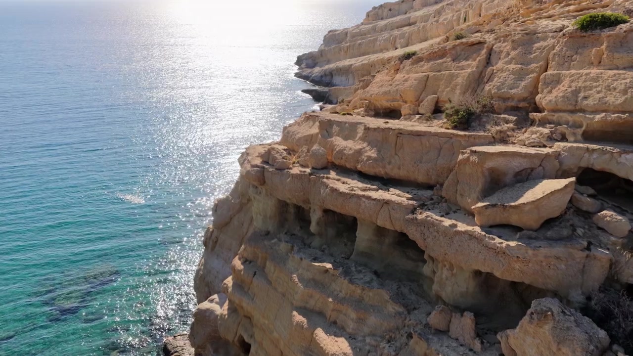 Vista aerea con drone di terrazze erose di arenaria chiara lungo una scogliera costiera sopra il mare aperto, Matala, Grecia