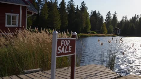 sale sign resting on wooden pier beside tranquil lake, waterfront houses nestled among forested shoreline under bright sunlight, depicting serene real estate landscape