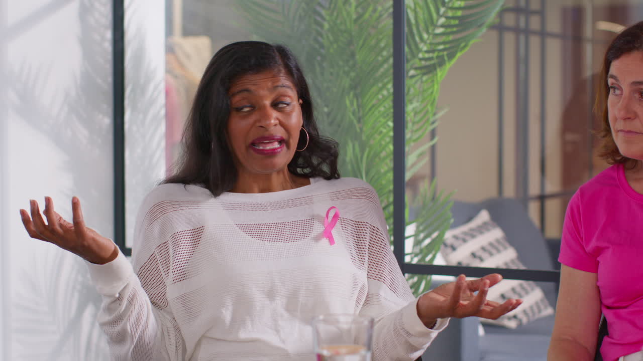 Mature Woman Wearing Pink Breast Cancer Awareness Ribbon Talking At Meeting Of Therapy Support Group For Cancer Treatment Patients 1