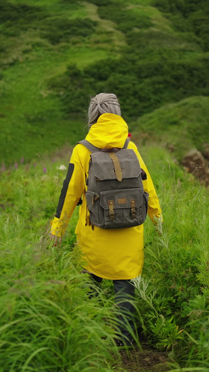 Woman in Yellow Raincoat Walking Through Tall Green Grass