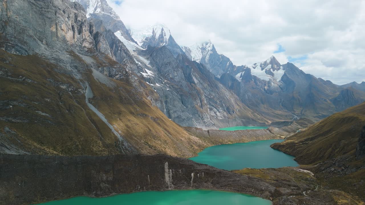 A majestic, slow-moving aerial shot flies over Tres Lagunas viewpoint on the Huayhuash trek, showing three turquoise glacial lakes below the majestic Yerupajá and Siula Grande peaks