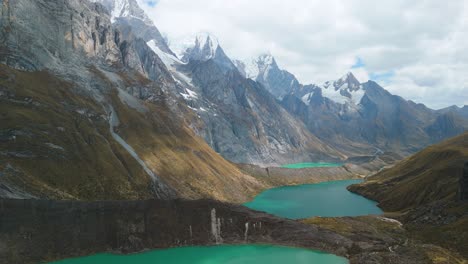a majestic, slow-moving aerial shot flies over tres lagunas viewpoint on the huayhuash trek, showing three turquoise glacial lakes below the majestic yerupajá and siula grande peaks