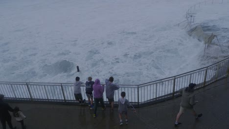 kids leaning on the metal railings watching the rough waves at the bronte beach - water overflowing at bronte rock pool during storm - sydney, nsw, australia