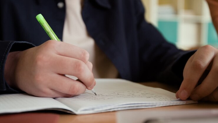 Close-up of a person writing in a notebook with a pen