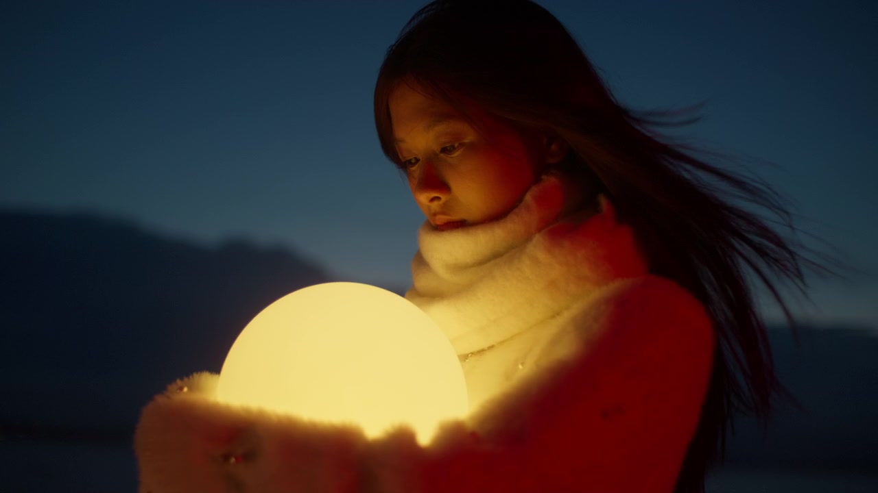 Giovane donna guarda un globo luminoso tenuto vicino al crepuscolo, esprimendo meraviglia e desiderio mentre il vento le soffia dolcemente tra i capelli