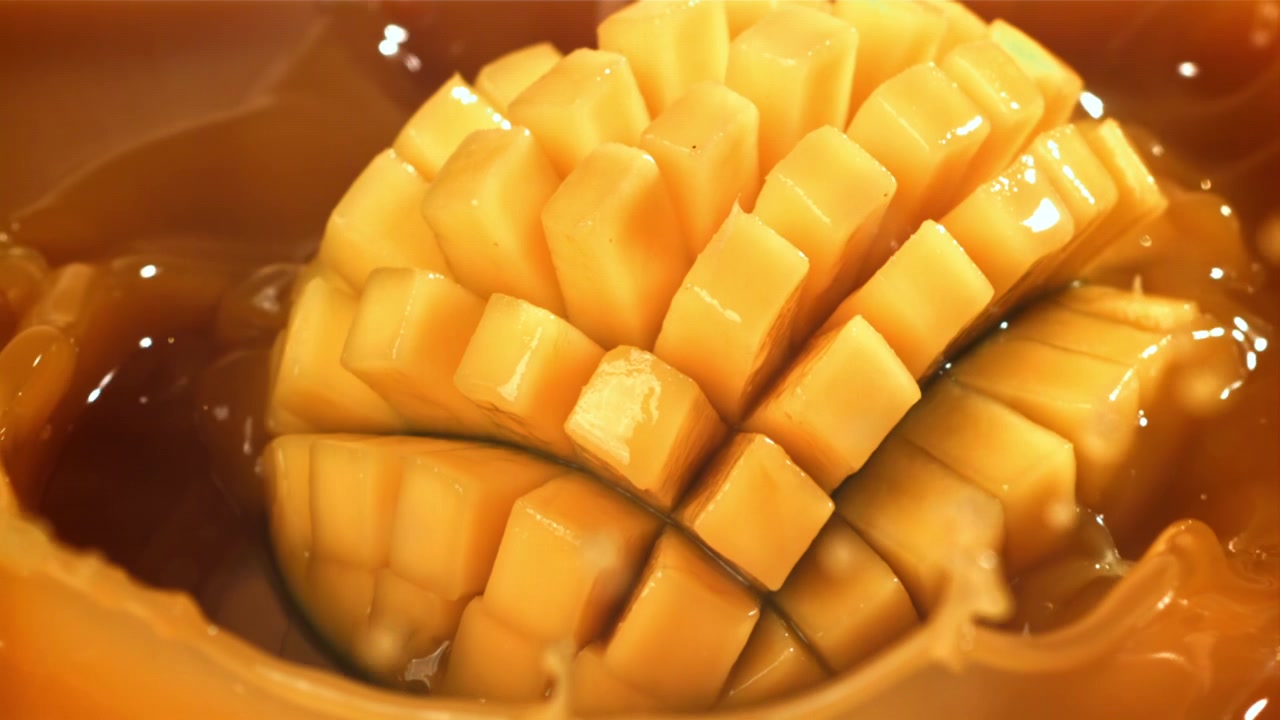 Mango fresco tagliato che si tuffa in succo tropicale dolce al rallentatore.