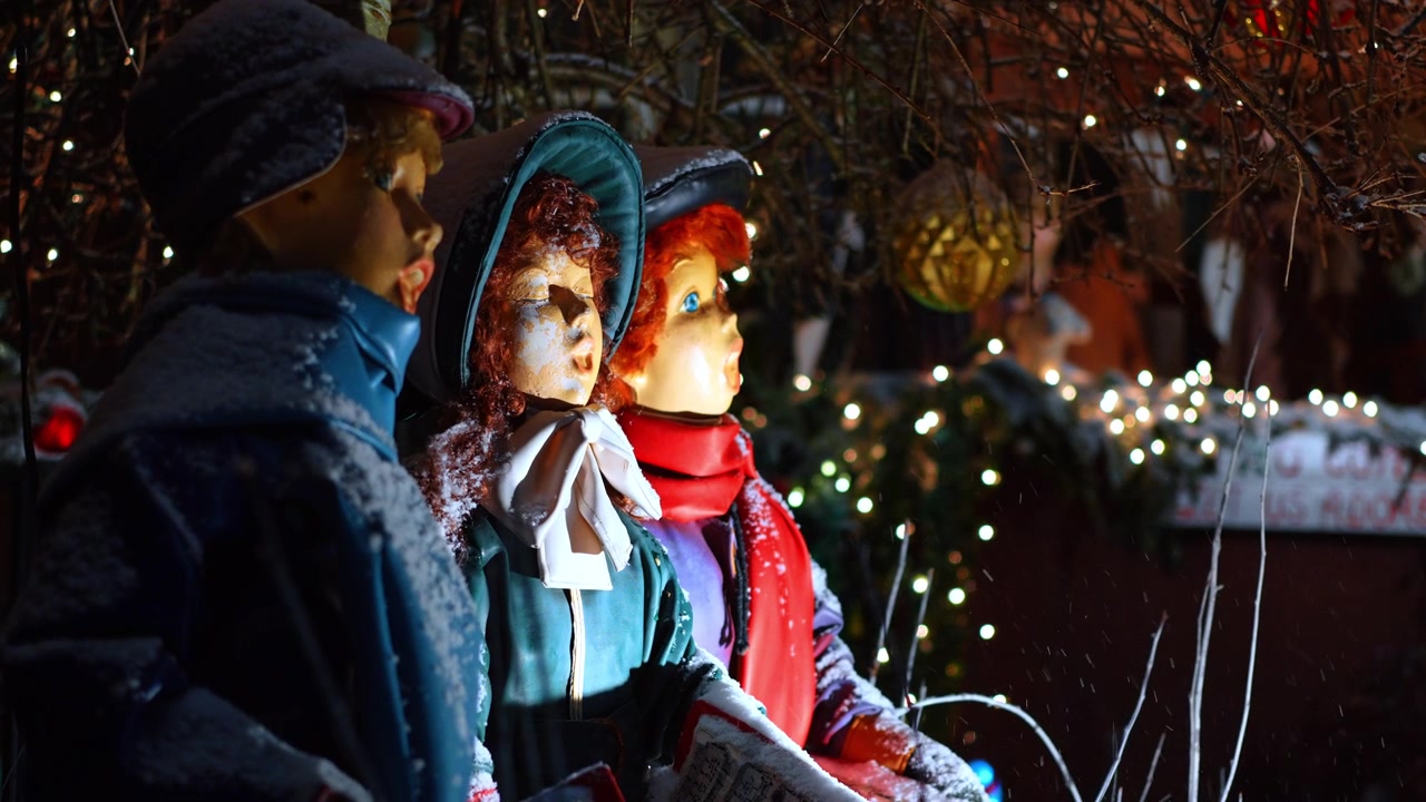 Vista laterale di tre figure di cantori natalizi in abiti invernali. Primo piano di profilo di cantori natalizi con spolverata di neve e calde luci bokeh a New York