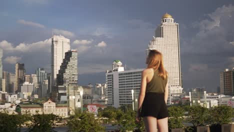 a young woman is admiring the blue sky and the city skyline of downtown bangkok