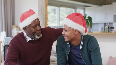 Feliz-Padre-E-Hijo-Afroamericanos-Con-Sombreros-Navideños-Teniendo-Videollamadas-Y-Abrazándose,-Cámara-Lenta