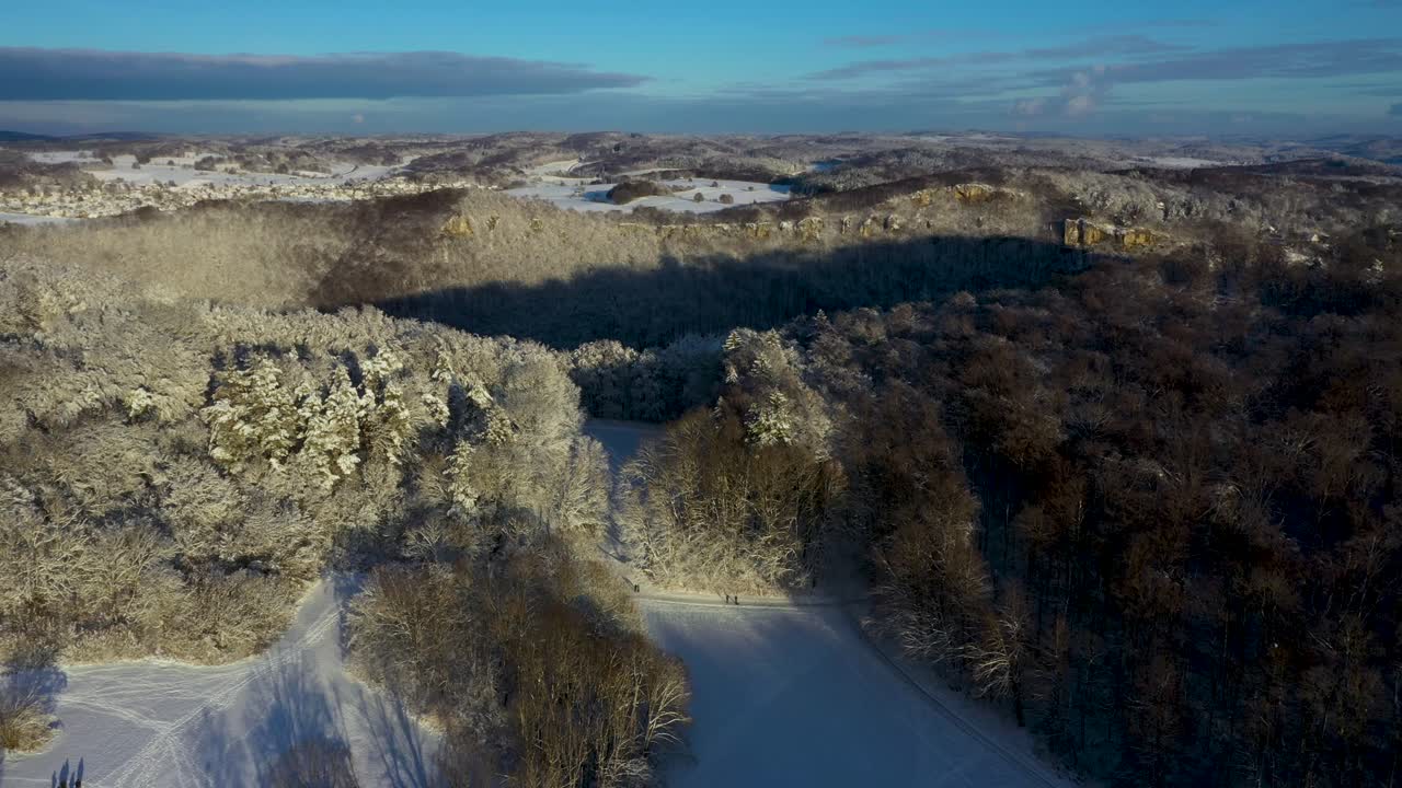 vuelo aéreo a través de montañas cubiertas de nieve y bosques con cielo azul durante el invierno en suabia, alemania
