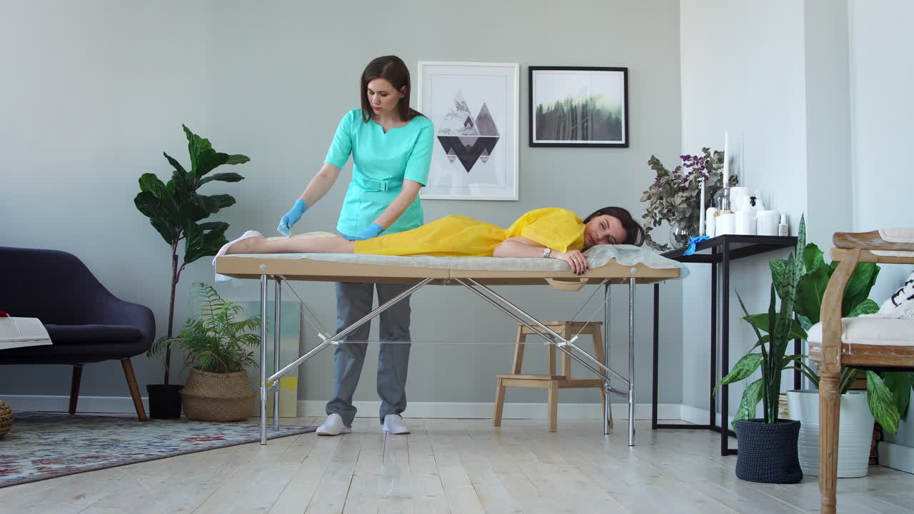 la chica habla por teléfono y sonríe durante la depilación de las piernas en el salón de belleza. depilación de las piernas con azúcar. maestro de depilación