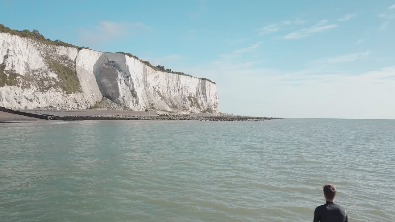 도버의 하얀 절벽과 푸른 하늘을 배경으로 바다를 바라보며 패들보드에 서 있는 청년