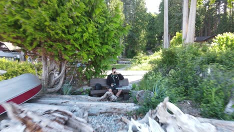 Young-man-sitting-on-a-bench-drinking-coffee-right-at-a-pebble-beach-on-Canada's-sunshine-coast