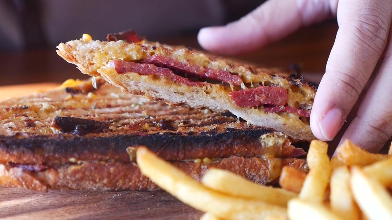 Mano che prende un panino con salsiccia grigliata e patatine fritte