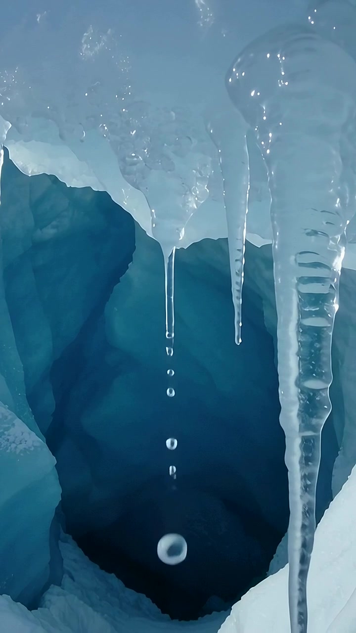 Video vertical: Racimo de carámbanos derritiéndose soltando gotas en una cavidad glacial, con carámbano estriado