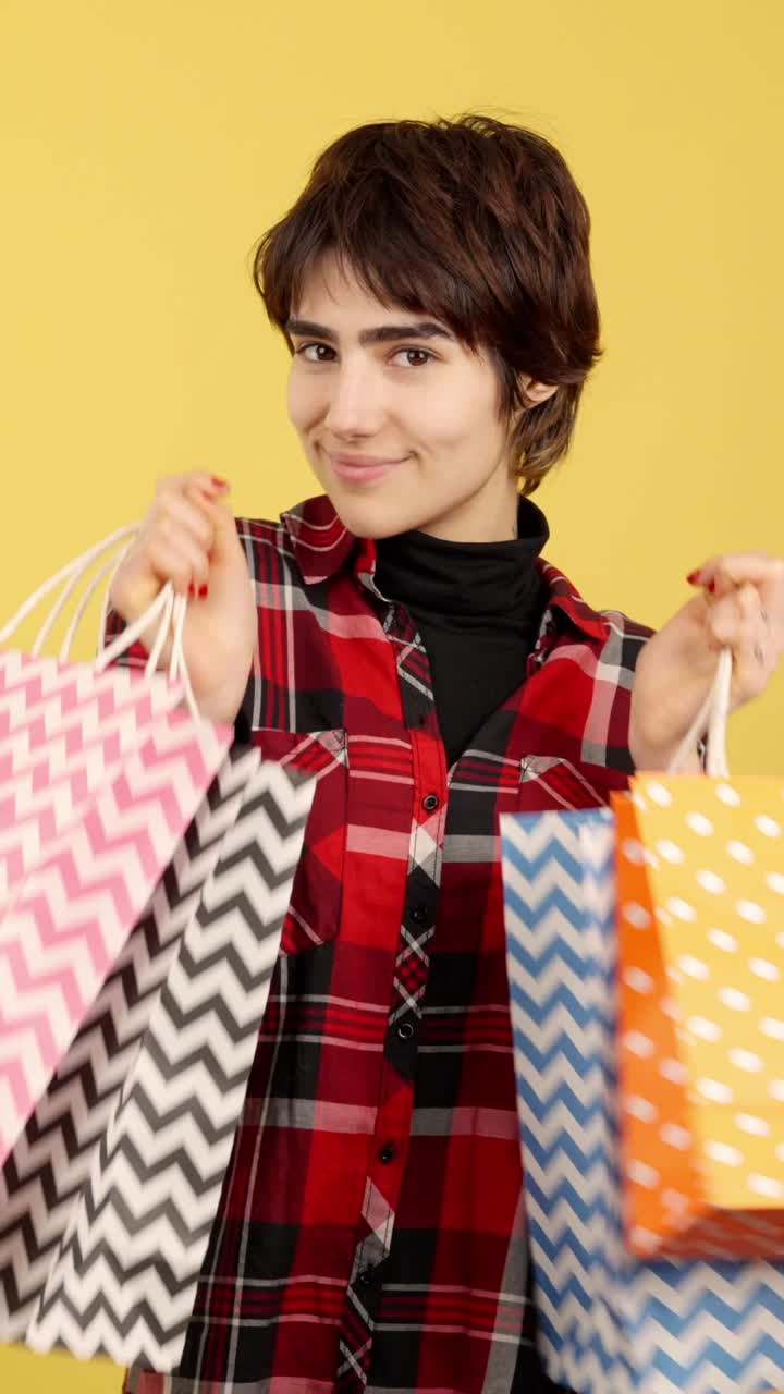 A young person happily holding colorful shopping bags against a yellow background
