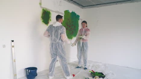 man and woman in workwear paint each other with sprays