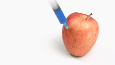 una jeringa en cámara súper lenta cayendo sobre una manzana