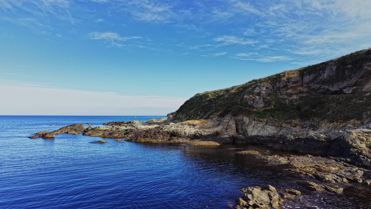 Scenic aerial view of rocky coastline meeting calm waters under blue sky