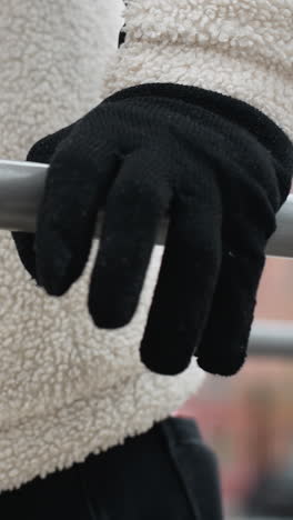vista lateral de un individuo con chaqueta blanca de invierno y guantes negros realizando flexiones al aire libre con un fondo de invierno borroso y figuras poco claras de personas caminando en clima frío