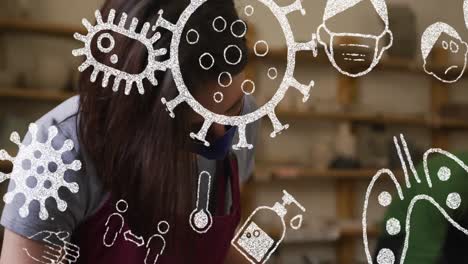 animation of virus icons over caucasian woman with face mask forming pottery