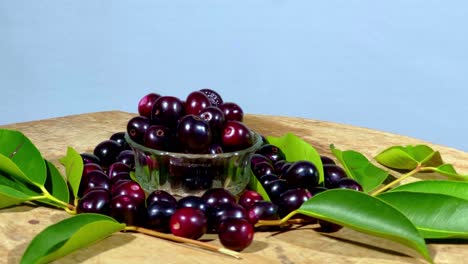 fresh jamun fruits in a bowl and jamun leaves on a rotating wooden table