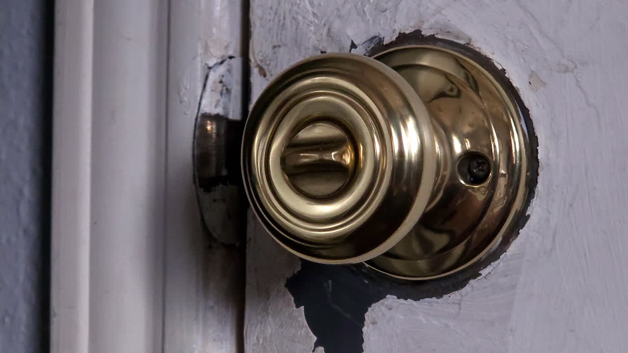 A scratched brass doorknob on an old wooden door slowly turns left and right