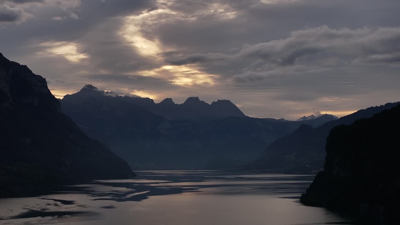 Silhouettes of mountains rising to the cloudy sky above Lake Walensee in Switzerland. Tranquil Swiss landscape at sunset