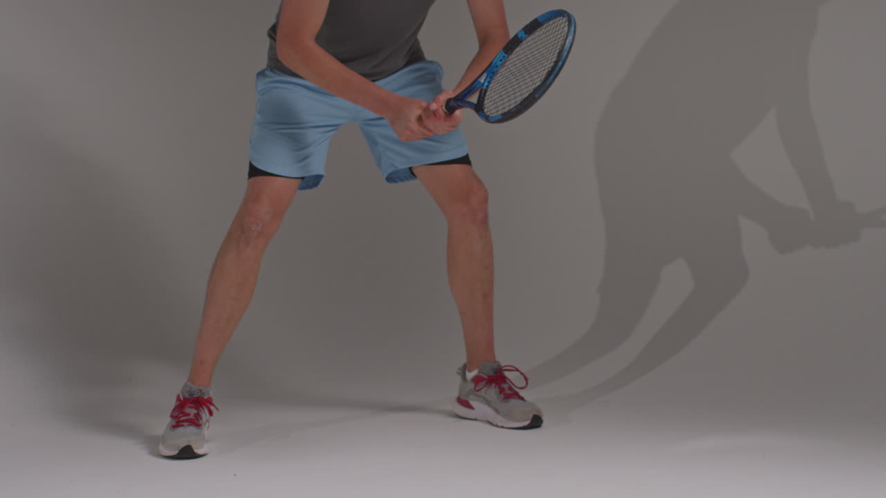 회색 배경에 공을 때리기 위해 라켓을 들고 기다리는 남자 테니스 선수의 다리에 대한 클로즈업 스튜디오