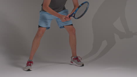 fotografía de estudio de cerca de las piernas de un jugador de tenis masculino con una raqueta esperando para golpear la pelota contra un fondo gris