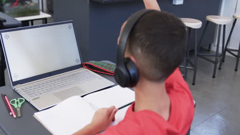 biracial boy with headphones studies at a laptop in a classroom in school with copy space