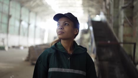 portrait of a young african-american woman checks a conveyor belt at a recycling plant. pollution control