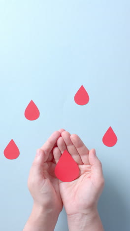 vertical video of hands of caucasian man holding blood drop on blue background with copy space