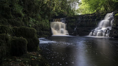 Lapso-De-Tiempo-De-La-Cascada-Del-Bosque-De-Primavera-Oscura-Rodeada-De-árboles-Con-Rocas-En-Primer-Plano-En-El-Paisaje-Rural-De-Irlanda