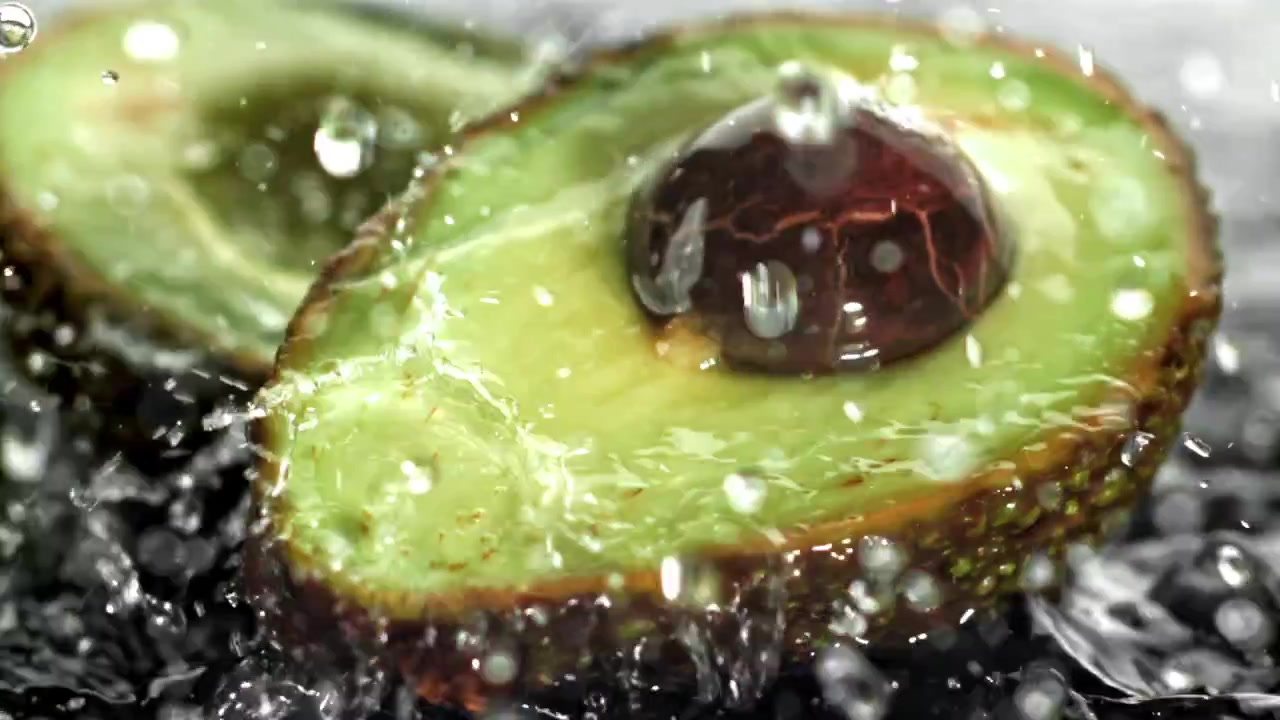 Acqua che schizza su mezzo avocado fresco con nocciolo